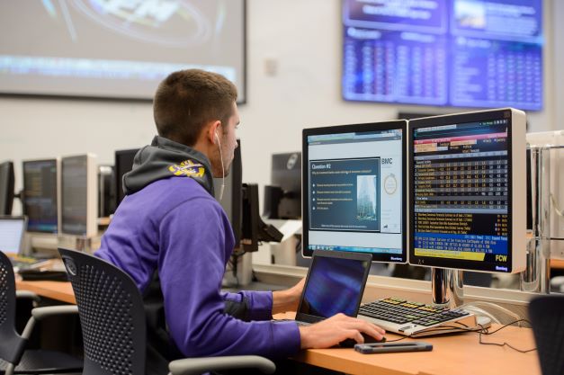 student studies financial data on a computer with two monitors